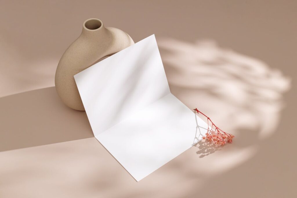 Elegant beige vase with blank card and dried flowers on a pink background.