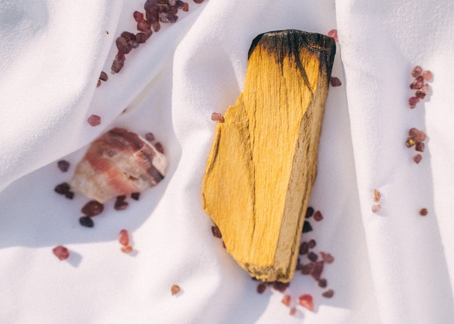 Palo Santo stick and rose quartz crystal scattered on white fabric with small pink stones.